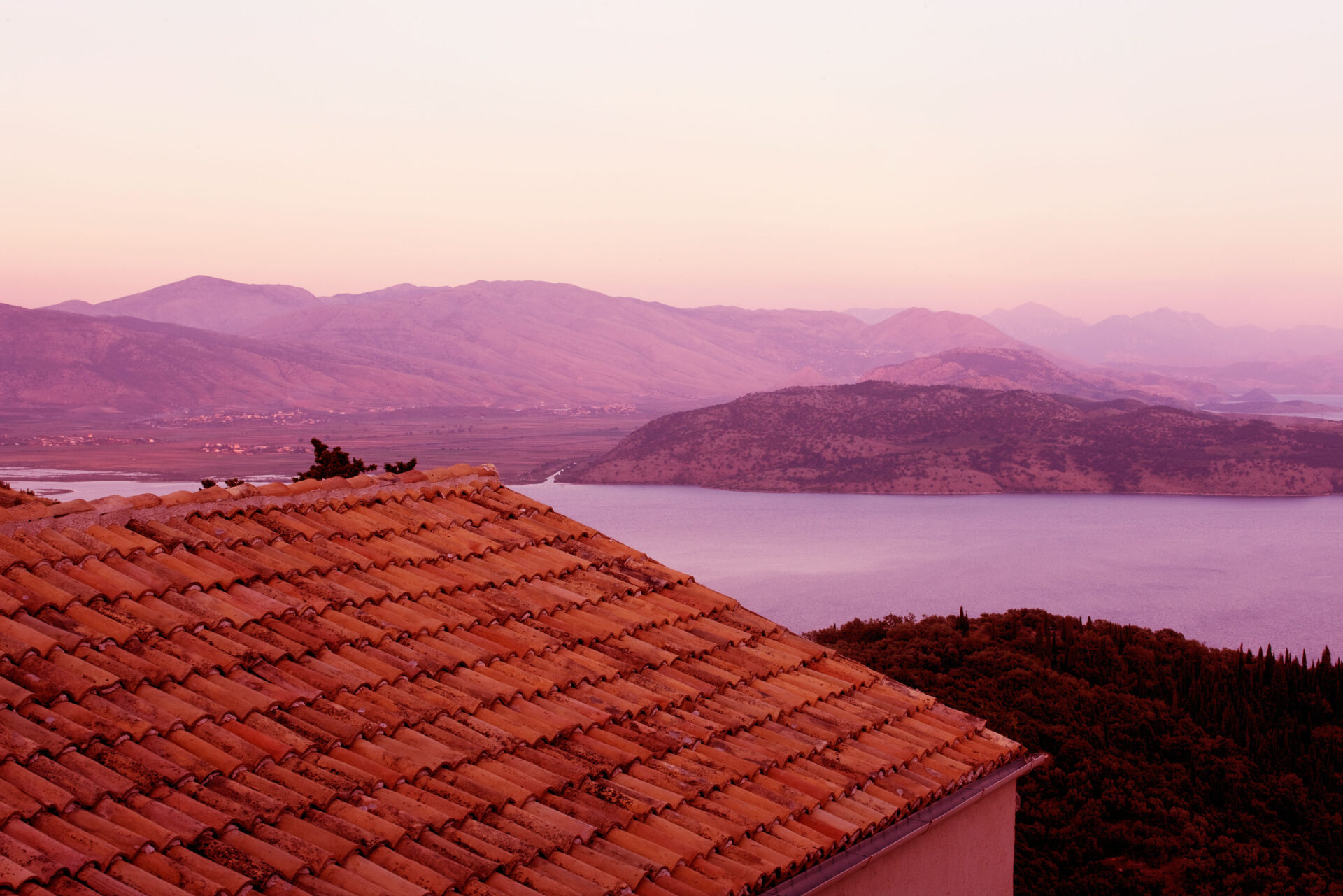 THE ROU ESTATE, CORFU, GREECE: DESIGNER: DOMINIC SKINNER - VIEW OVER HOUSE ROOF TO ALBANIAN MOUNTAINS AT DAWN